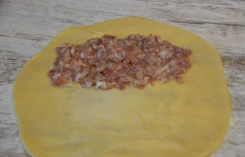 1. Этап. Чебуреки из говядины: При работе с заварным тестом рабочую поверхность стола уже не надо припылять мукой. Раскатайте тесто в пласт, выложите на одну половину фарш, равномерно распределяя по тесту.