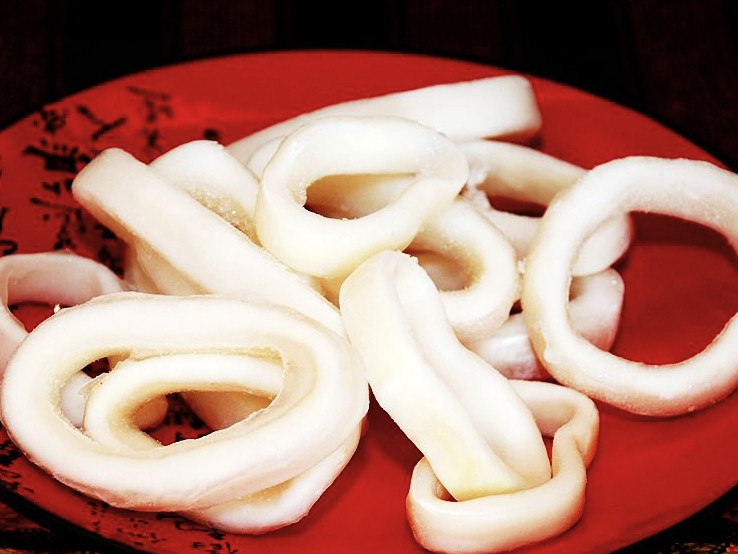 1. Этап. Кальмары в масле: Тушки кальмара промойте, очистите и нарежьте кольцами. Кольца не делайте толщиной более 7-8 миллиметров. В противном случае они не смогут прожариться и будут твёрдыми. Кольца залейте кипятком на 3-4 минуты.