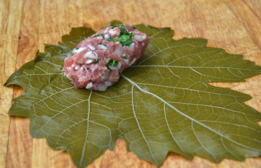 1. Этап. Долма с бараньим фаршем: 8. Разделите фарш на части, выложите небольшое его количество на верхнюю часть виноградного листа, затем заверните фарш.