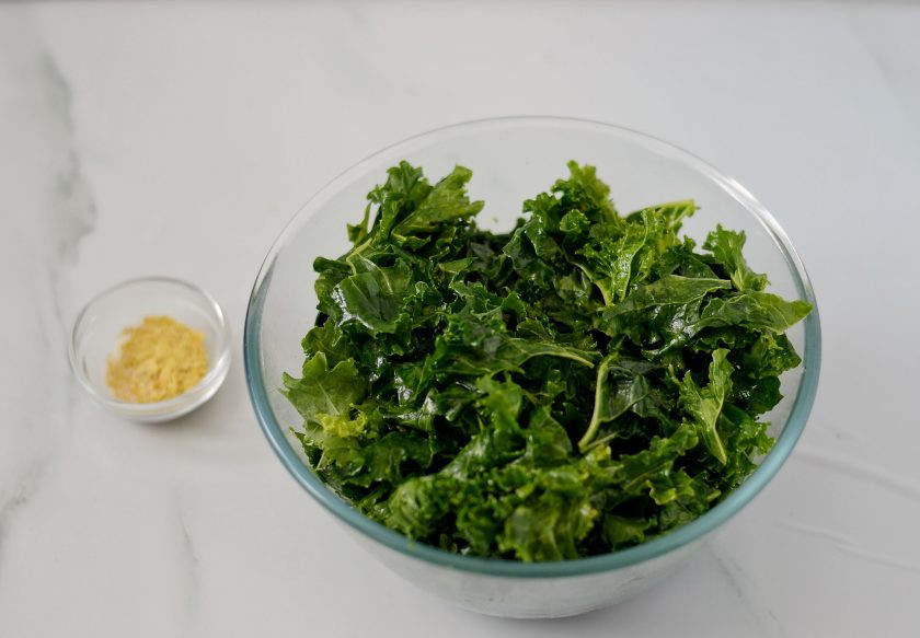 1. Этап. Чипсы из кейла: Переложите кейл в глубокую миску, полейте маслом и начните руками сжимать листья, чтобы они стали мягче.