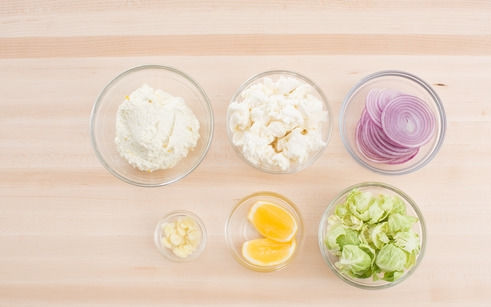 1. Этап. Пицца с творогом: 1. Подготовьте все ингредиенты: очистите и нарежьте кольцами лук. Натрите цедру и добавьте в творог. Моцареллу разомните, измельчите чеснок. Вымойте и обсушите брюссельскую капусту и рукколу.