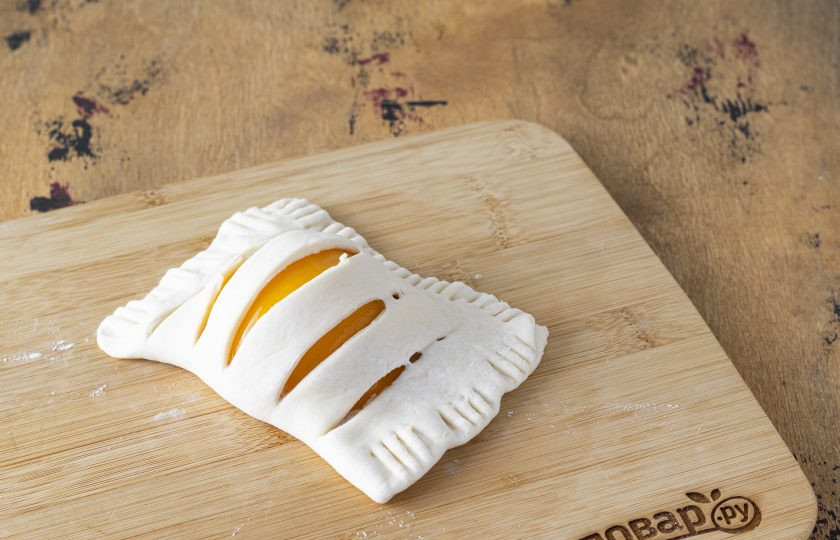 1. Этап. Слойки с консервированными персиками: Сложите тесто пополам, края защипните вилкой.