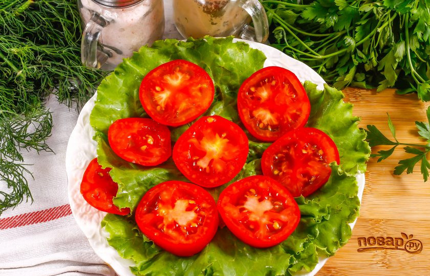 1. Этап. Салат с тунцом и яйцом пашот: Промойте помидоры в воде, срежьте зеленые сердцевинки, нарежьте их кольцами и выложите на листья салата.