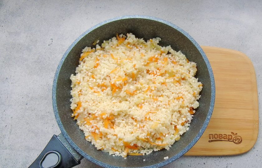 1. Этап. Окорочка с рисом в духовке: Рис тщательно промойте в проточной воде Выложите в сковороду с луком и морковью. Перемешайте и жарьте с овощами 3-4 минуты.