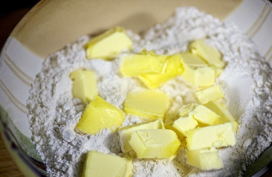 1. Этап. Яблоки, запеченные в тесте: 1. Для начала нужно приготовить тесто. Для этого в глубокую мисочку просейте муку и добавьте холодное сливочное масло, нарезанное небольшими кубиками.