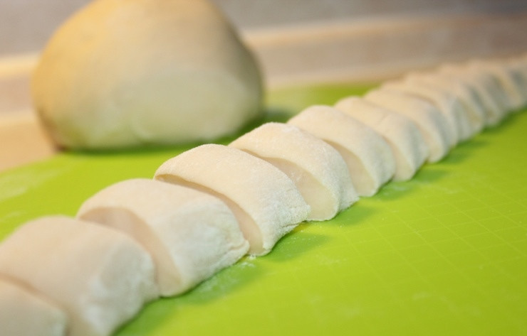 1. Этап. Вареники с сырой картошкой: В просеянной муке делаем небольшое углубление и вливаем в него молоко, воду и растительное масло, разбиваем яйцо, добавляем соль. Тщательно вымешиваем тесто до однородной консистенции, если оно получается не достаточно плотным и эластичным, можно добавить еще немного муки. Даем тесту постоять 10-15 минут под полотенцем, а затем разделяем его на несколько частей, каждую часть скатываем в колбаску и разрезаем ее на небольшие кусочки, формируем из них шарики.