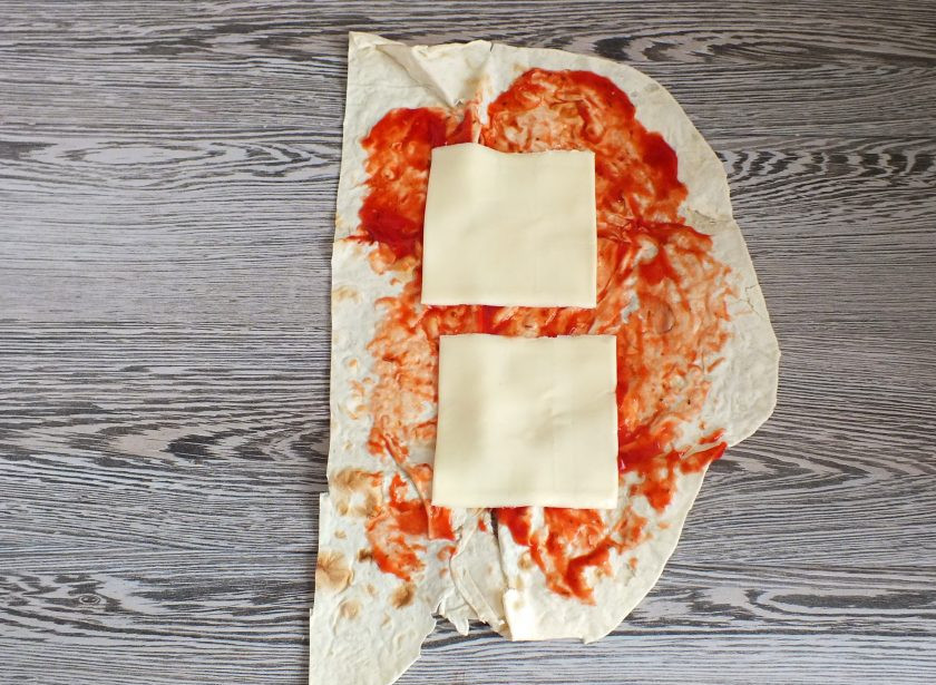 1. Этап. Бургер в лаваше: Возьмите одну полосу из лаваша. Смажьте кетчупом, выложите по две пластинки сыра.