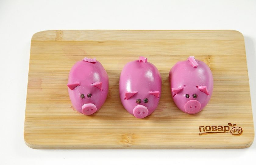 1. Этап. Закуска Поросята: Переверните яйца начинкой вниз. Из срезанного ранее окрашенного белка вырежьте ножом ушки в виде треугольника, пятачки и хвостики. Глазки сделайте из перца горошком. Пятачок, чтобы держался, смажьте с одной стороны слегка начинкой или майонезом. Ушки и хвостик вставьте в продольное отверстие, сделанное ножом.