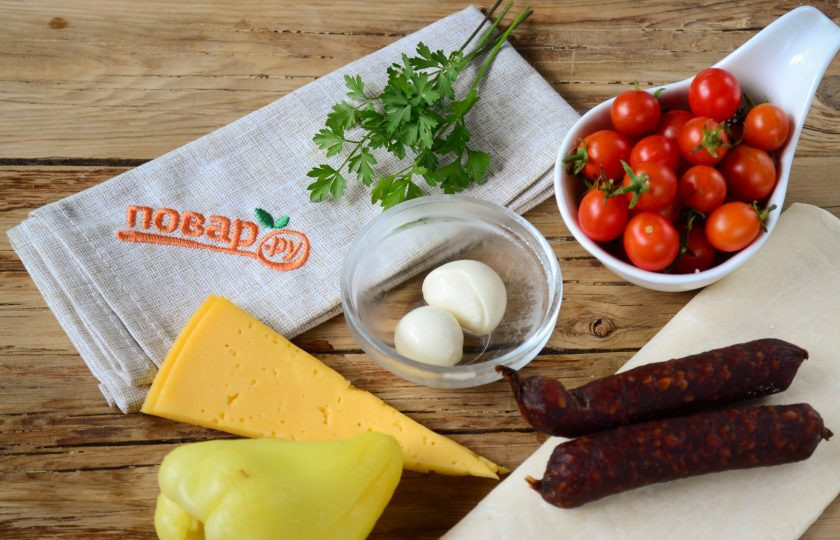 1. Этап. Пицца на шпажках в духовке: Подготовьте все необходимые ингредиенты. Очистите и ополосните сладкий перец, затем нарежьте его на небольшие квадратики. Мини-пепперони порежьте на кружочки толщиной 7-8 мм, твердый сыр также порежьте на квадратики. Необходимое количество теста разморозьте и порежьте на плоски шириной 2 см.