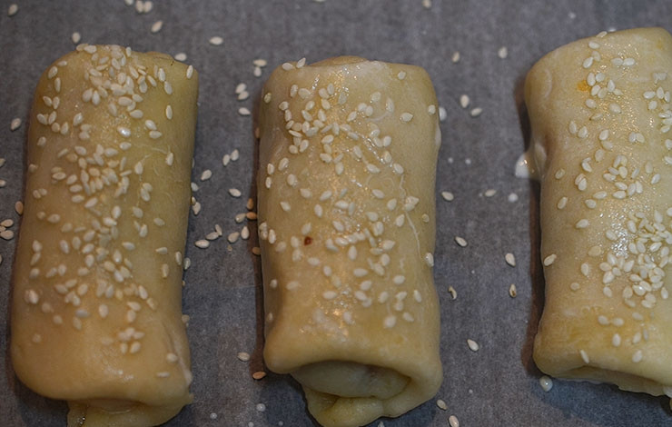 1. Этап. Закусочные трубочки с курицей и овощами: Выложите на противень. Смажьте желтом и посыпьте кунжутом.