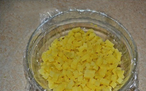 1. Этап. Салат для праздничного стола: Отвариваем картофель в мундирах, остужаем, а затем нарезаем небольшими кубиками. Застилаем глубокую салатницу пищевой пленкой и выкладываем слой из картофеля.