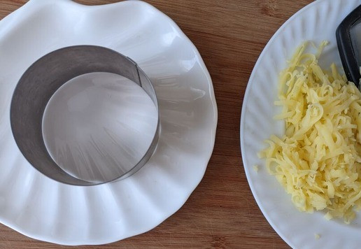 1. Этап. Салат Кудрявый Ваня: Так как этот салат слоёный, то для удобства его приготовления, можно взять большое разъёмное кольцо или готовить в маленьких кулинарных кольцах для порционной подачи. Кольцо кладём на блюдо (тарелку). Для нижнего слоя берём вареный картофель, чистим, трём на тёрку.