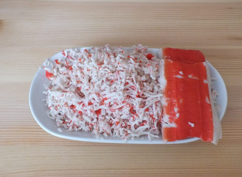 1. Этап. Закуска новогодняя Мышки с крабовыми палочками: Возьмите 3-4 шт. крабовых палочки и снимите с них красную часть. После все крабовые палочки натрите на мелкой терке. 1/4 часть от натертой массы отложите.