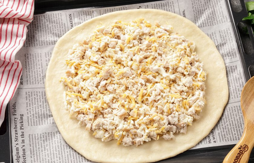 1. Этап. Бездрожжевой пирог с курицей: Большую часть теста раскатайте в форме круга на пергаменте и перенесите на противень. Сверху распределите начинку ровным слоем, отступив немного от края.