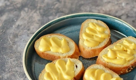 1. Этап. Бутерброды с селёдкой и помидорами: Багет нарежьте на ломтики и слегка подсушите их с двух сторон на сковороде без масла (или в тостере). Смажьте ломтики багета майонезным сырным соусом (или просто майонезом).