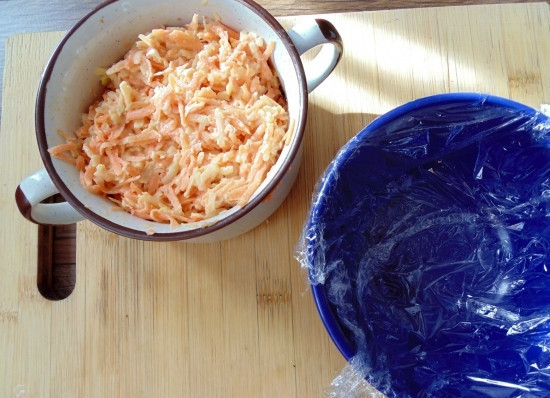 1. Этап. Салат Шапочка Деда Мороза: 5. Теперь можно начинать собирать салат. Небольшую круглую салатницу застелите пищевой пленкой. Выложите на дно морковь с яблоком и разровняйте.