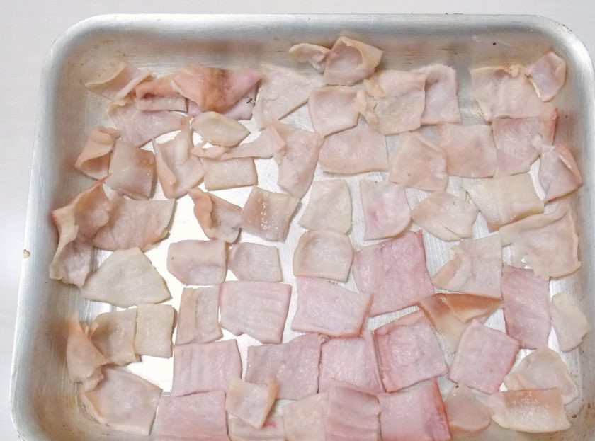 1. Этап. Чипсы из свиной шкурки: Свиную шкурку разрежьте на кусочки примерно 3 на 3 сантиметра. Выложите на противень прослойкой сала вверх.