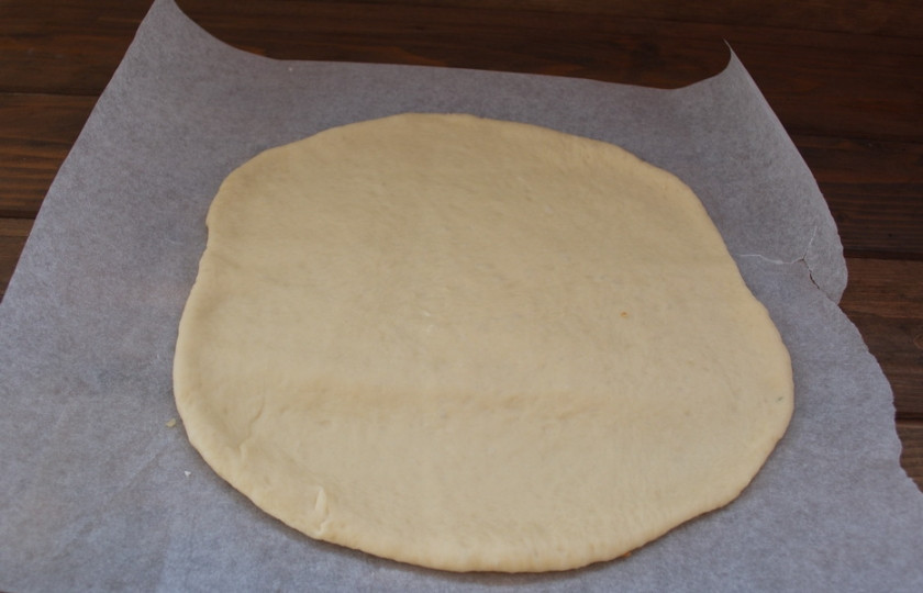 1. Этап. Пирог с зеленью и брынзой: Разделите тесто на две половинки. Одну половинку отложите. Вторую раскатайте на листе пергамента для выпечки.