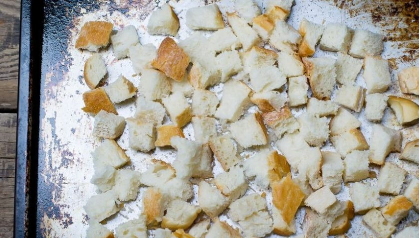 1. Этап. Курятина в духовке: Хлеб нарежьте на небольшие кубики. Прекрасно подойдет для этого белый багет. Смажьте противень растительным маслом, выложите на него хлеб, распределив равномерно.