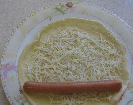 1. Этап. Блины с сосиской: 3. Блинчик разложить на тарелке и присыпать тертым сыром. Сосиски предварительно вымыть, просушить и очистить. При желании их можно отварить или обжарить на сковороде (или на гриле). Выложить на край блинчика. Рецепт приготовления блинов с сосиской можно дополнить горчицей или томатным соусом, например.