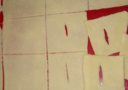 1. Этап. Хворост тонкий хрустящий без водки: Раскатываем тесто на обсыпанной мукой разделочной доске или прямо на столе. Толщина должна быть минимальная, ведь мы хотим получить тонкий и воздушный хворост. Нарезаем пласт теста на небольшие квадратики, а в середине каждого делаем прорезь.