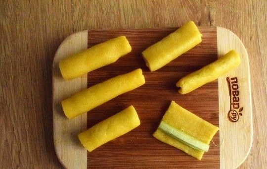 1. Этап. Печенье с ревенем: Духовку разогрейте до 160 °C. Раскатайте тесто в пласт толщиной 0,5 см. Нарежьте на полоски шириной 5-6 см. Положите кусочек ревеня, заверните тесто в один оборот, отрежьте остаток, немного прокатайте ладонью заготовку.