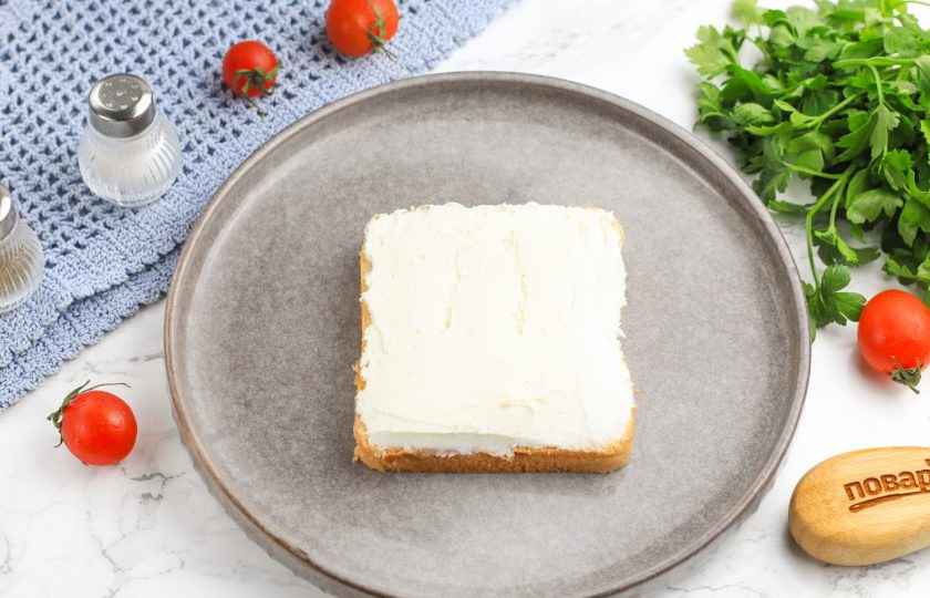 1. Этап. Канапе с семгой и икрой: Ломтик хлеба смажьте половиной творожного сыра, стараясь сделать слой как можно толще.