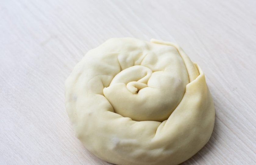 1. Этап. Слоеные лепешки с луком на сковороде: Скатайте тесто рулетом и скрутите в улитку.