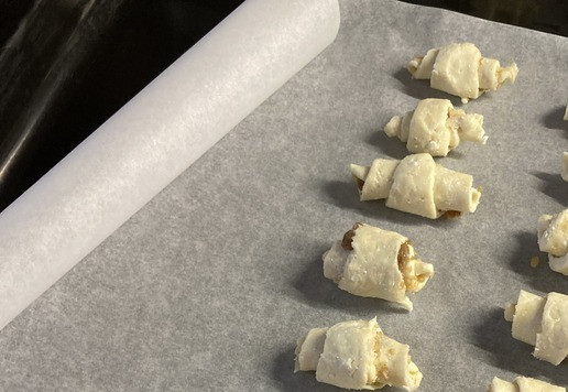 1. Этап. Творожные мини-рогалики с орехом и изюмом: Завернуть каждую из 16 частей в рогалик (от широкой части к узкой), выкладывая на противень, покрытый бумагой для выпечки.