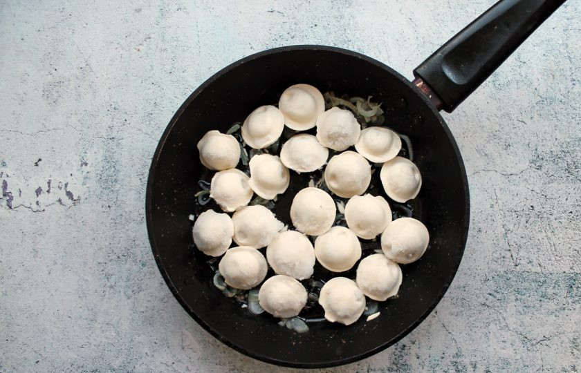 1. Этап. Жареные пельмени с луком на сковороде: Замороженные пельмени выложите на репчатый лук в один слой, посолите и поперчите. Сделайте медленный огонь, закройте сковороду крышкой и обжаривайте все в течение 10 минут, перемешивая 2-3 раза.