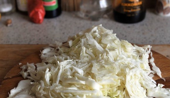 1. Этап. Кимчи из белокочанной капусты: С кочана капусты снимите верхние листья. Затем нашинкуйте ее на тонкие полоски. Удобнее всего это делать при помощи терки или кухонного комбайна со специальными насадками.