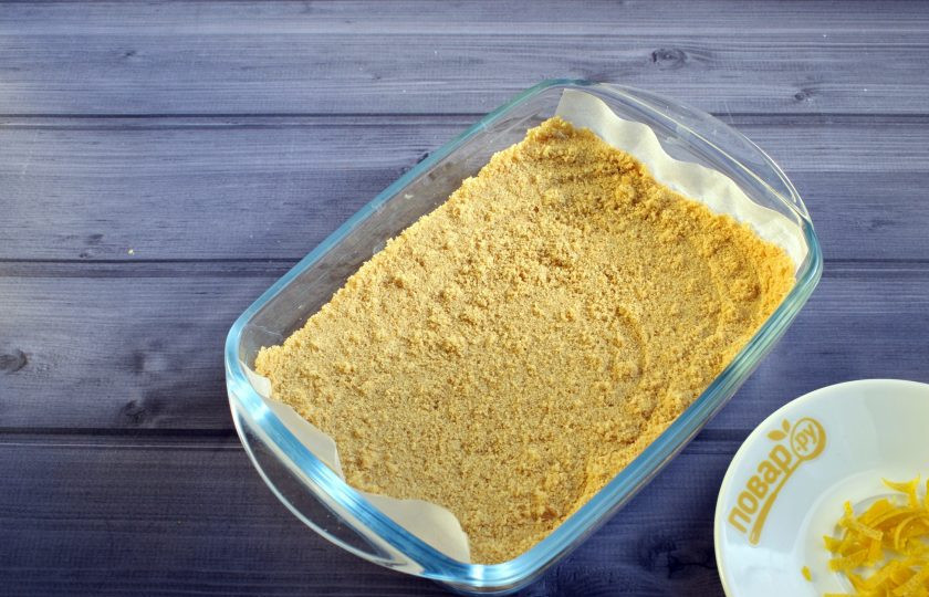 1. Этап. Ароматный лимонный чизкейк: Печенье измельчите в крошку. На дно формы (14х18 см) постелите пергамент для выпечки. Утрамбуйте крошку печенья по дну формы.