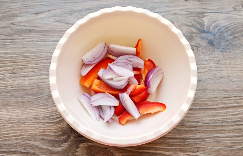1. Этап. Радужная форель в духовке с овощами: Красный лук почистите и разрежьте вдоль на 6-8 частей. Добавьте его в миску с перцем.