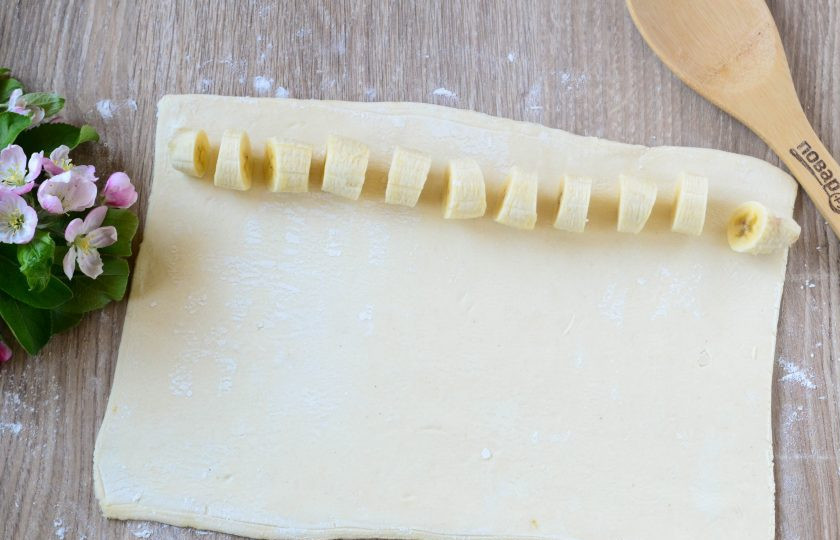 1. Этап. Шоколадное кольцо: Тесто тонко раскатайте в форме прямоугольника примерно 30 на 25 см. Вдоль длинной стороны выложите кружочки бананов.