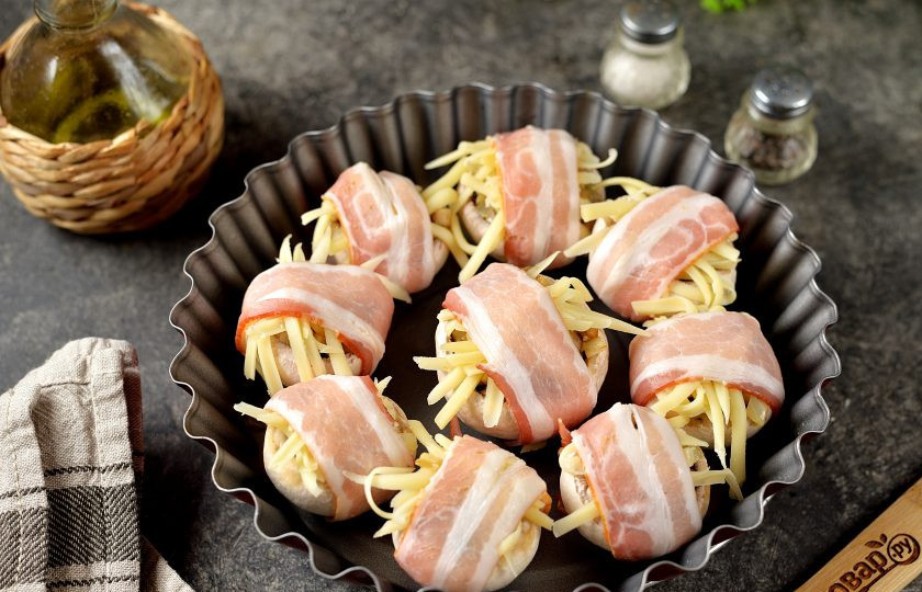 1. Этап. Шампиньоны в беконе в духовке: Замотайте каждую нафаршированную грибную шляпку в ломтик сыровяленого бекона, переложите в удобную огнеупорную форму. Отправьте заготовки в предварительно разогретую до 190 градусов духовку на 20-25 минут. Противень установите ровно посередине духовки, следите, чтобы бекон не сильно подсушился.