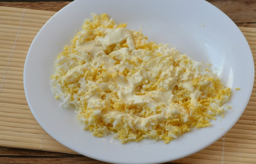 1. Этап. Салат с тунцом: Салат выкладывайте в форме полукруга. Первым слоем натрите яйца, отложив белок одного яйца. Он нам ещё понадобится для украшения. Смажьте первый слой майонезом.