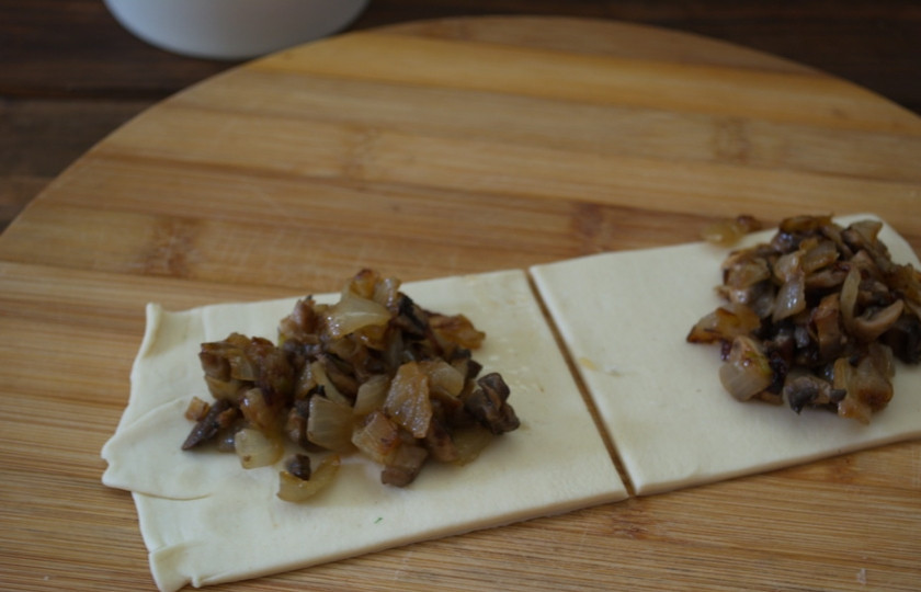 1. Этап. Пирожки с белыми грибами: Слоеное тесто раскатайте в пласт. Нарежьте на квадратики. На центр каждого выложите подготовленную начинку. Соедините два противоположных края, придав пирожку форму треугольника.