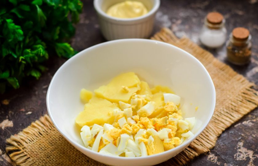 1. Этап. Оливье с горбушей: Вареные картофель и яйца нарежьте небольшими кубиками и сложите сразу в салатник.