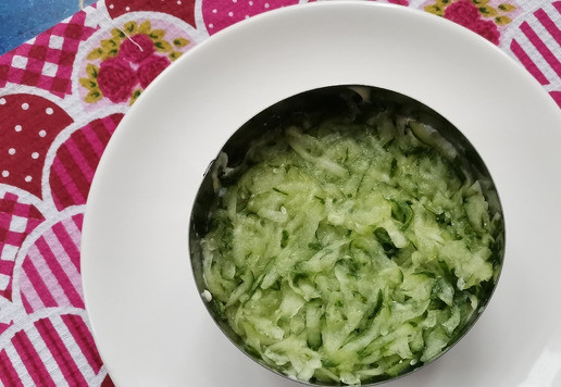 1. Этап. Слоёный рыбный салат Лето: Свежий огурец вымыть, обсушить бумажным полотенцем и натереть на крупной тёрке. Затем отжать (!) и распределить ровным слоем внутри формочки. Майонезом смазывать не нужно!