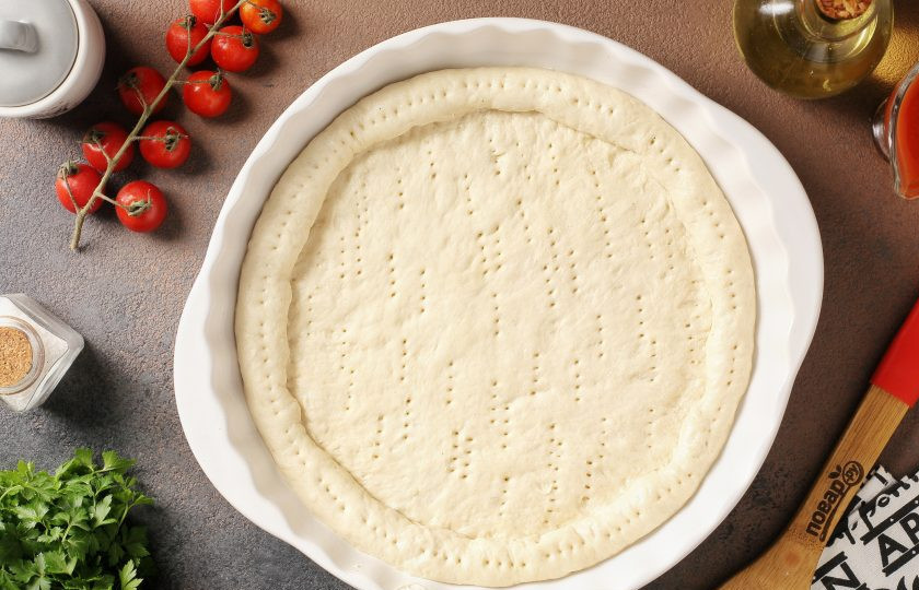 1. Этап. Пицца из дрожжевого теста холодного приготовления: Тесто раскатайте и выложите в смазанную маслом форму, сформируйте руками бортики желаемой высоты и наколите тесто по всей поверхности вилкой.