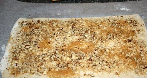 1. Этап. Печенье из слоеного теста: Посыпаем тесто измельченными орехами и сахаром. Слегка проходимся скалкой, чтобы орехи немного вдавились в тесто.