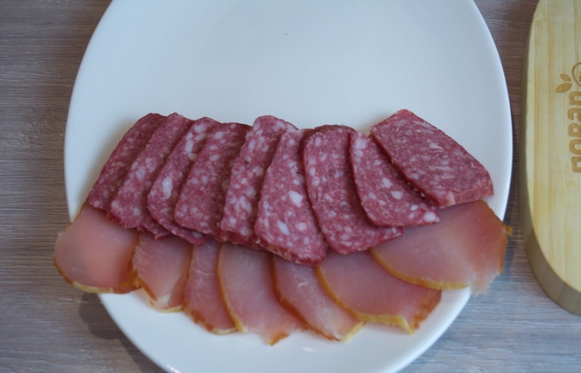 1. Этап. Мясная нарезка в виде ёлочки: Следующим слоем выложите колбасные изделия.