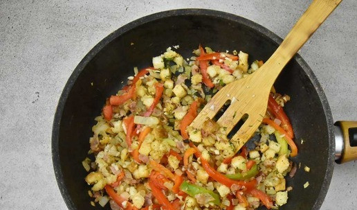 1. Этап. Рулет из индейки с беконом: В сковороду влейте масло, разогрейте и добавьте бекон. Обжарьте до вытапливания жира, переложите подготовленный репчатый лук и обжарьте до золотистости. Добавьте чеснок, хлебные кубики, обжарьте в течение 1-2 минут на среднем огне. В конце отправьте в сковороду измельченную зелень и соломку болгарского перца.