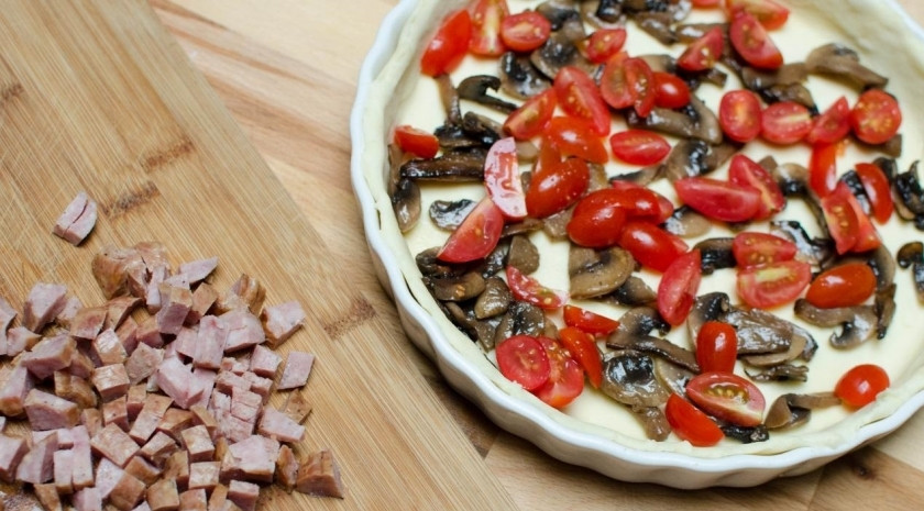 1. Этап. Киш с грибами и сыром: Помойте помидоры черри. Немного просушите их бумажной салфеткой или кухонным полотенцем. Разрежьте их на четвертинки и выложите к грибам в основу для киша. Колбасу мелко нарежьте и добавьте туда же.