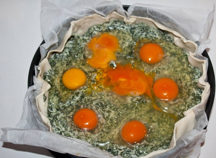 1. Этап. Пасхальный пирог со шпинатом и рикоттой: 2. Слоеное тесто раскатайте в пласт и уложите в форму для выпечки. Наколите тесто вилкой и, если используете ветчину, то положите ее на тесто. Теперь выложите половину начинки из шпината, сделайте в ней углубления для яиц. Вбейте яйца так, чтобы желтки остались целыми.