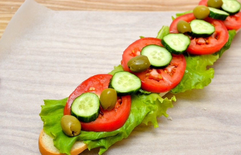 1. Этап. Cэндвич как в Сабвей: Пока верхушка запекается, на нижнюю часть багета выложите сначала листья салата, затем огурцы и помидоры (нарезанные кружочками) и оливки.