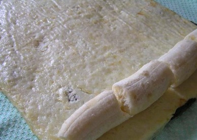 1. Этап. Шоколадный рулет с бананом: Посыпаем верх испеченного пласта сахарной пудрой и выкладываем шоколадным слоем вниз на полотенце или пергамент. На творожный слой с узкого края выкладываем очищенные бананы.