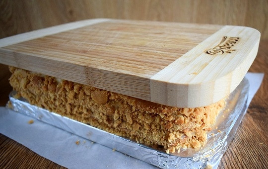 1. Этап. Медовое пирожное с начинкой: Последний корж не смазывайте. Корж из обрезков измельчите в крошку (средней величины) с помощью скалки или блендера, украсьте крошкой бока. Положите сверху груз, чтобы выравнять верхний корж, поставьте торт в холодильник на 3-4 часа, лучше — на ночь.