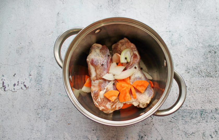 1. Этап. Фаршированные свиные калтыки: Калтыки сполосните и выложите в кастрюлю с толстым дном. Добавьте порезанные репчатый лук и морковь. Все посолите, добавьте черный перец горошком и налейте полтора литра воды.