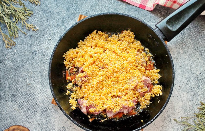 1. Этап. Кукурузная каша с тушенкой: Кукурузную крупу промойте в теплой воде, дайте стечь воде и высыпьте поверх тушенки и овощей.